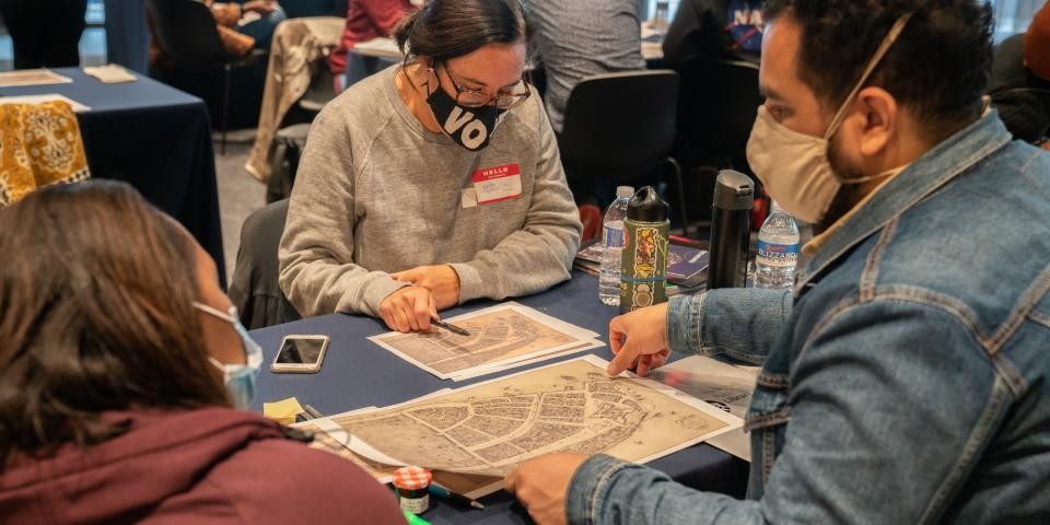Several people in face masks sit at a table and look at various historical maps together.