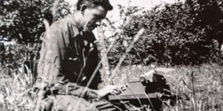 J. D. Salinger sits with a typewriter on a suitcase in a Normandy meadow