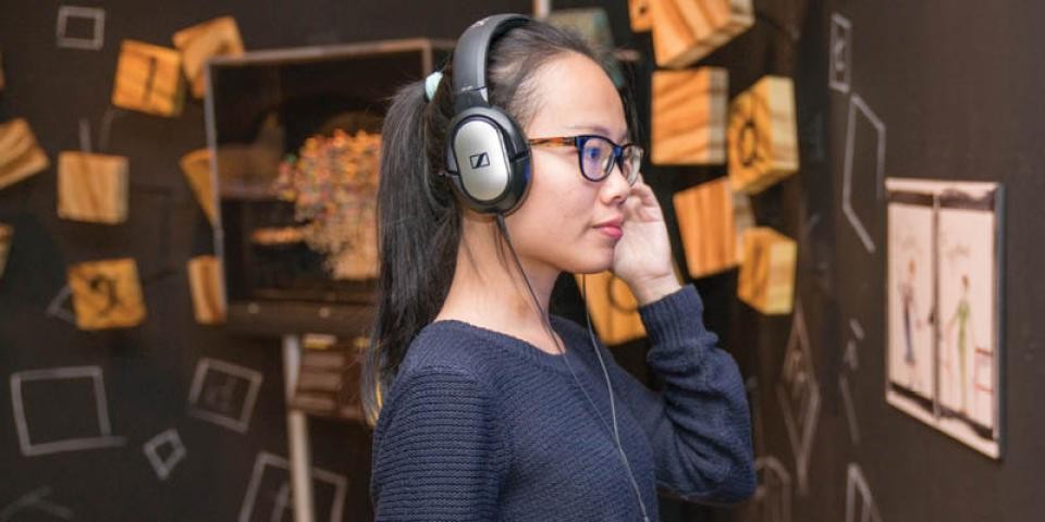A woman with glasses and over-ear headphones listens to music. 