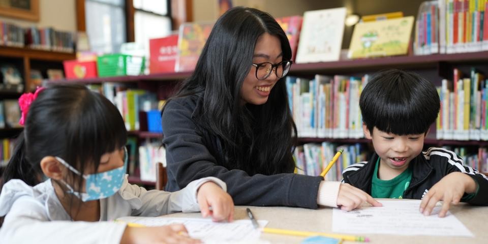A tutor helps two younger children with worksheets at Seward Park Library.