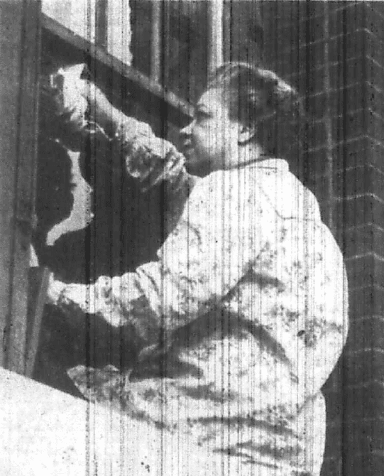 Journalist Marvel Cooke, seated on a window ledge outside of building washing window