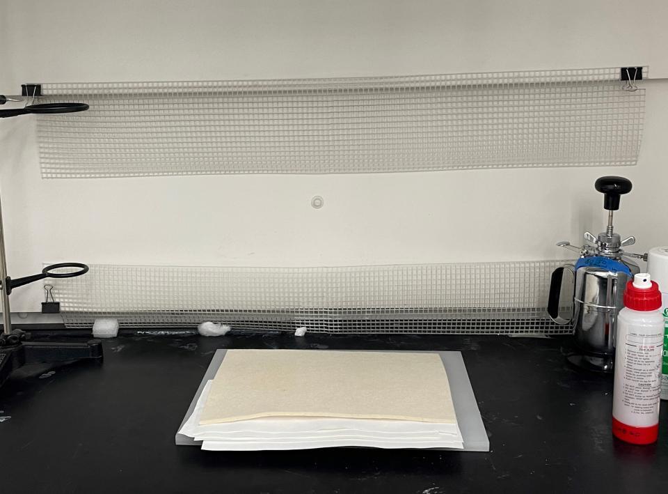 A stack of sheets of white TEK-WIPE fabric under an thick off-white rectangle of felt in a fume hood.