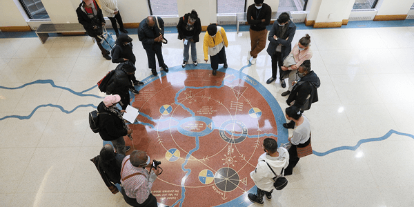 Photographer from above, a group of people are standing around the Schomburg Center’s cosmogram. 