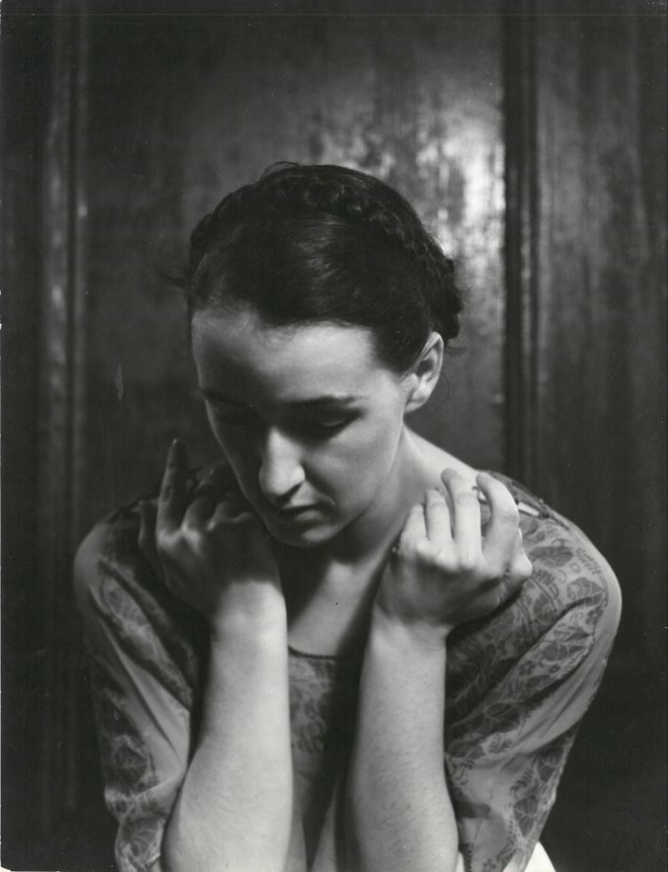 Portrait of a young woman looking down, hands held up to her face.