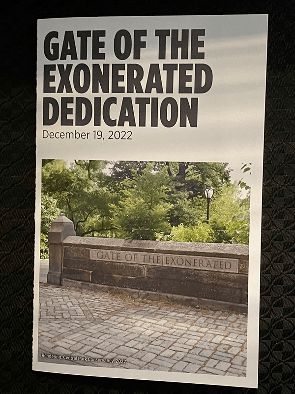 Against a black background, a white colored invitation. In black lettering, there are words Gate of the Exonerated Dedication, December 19, 2022. Below is a rendering of the gate, which is a stone entryway to the mark.