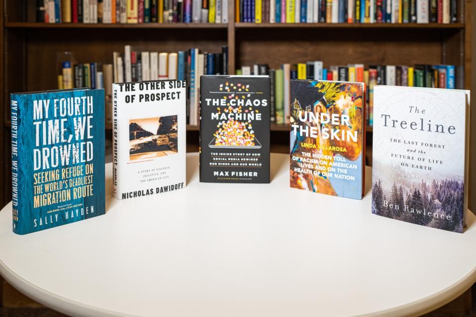 five books placed vertically on a round table in front of bookshelves