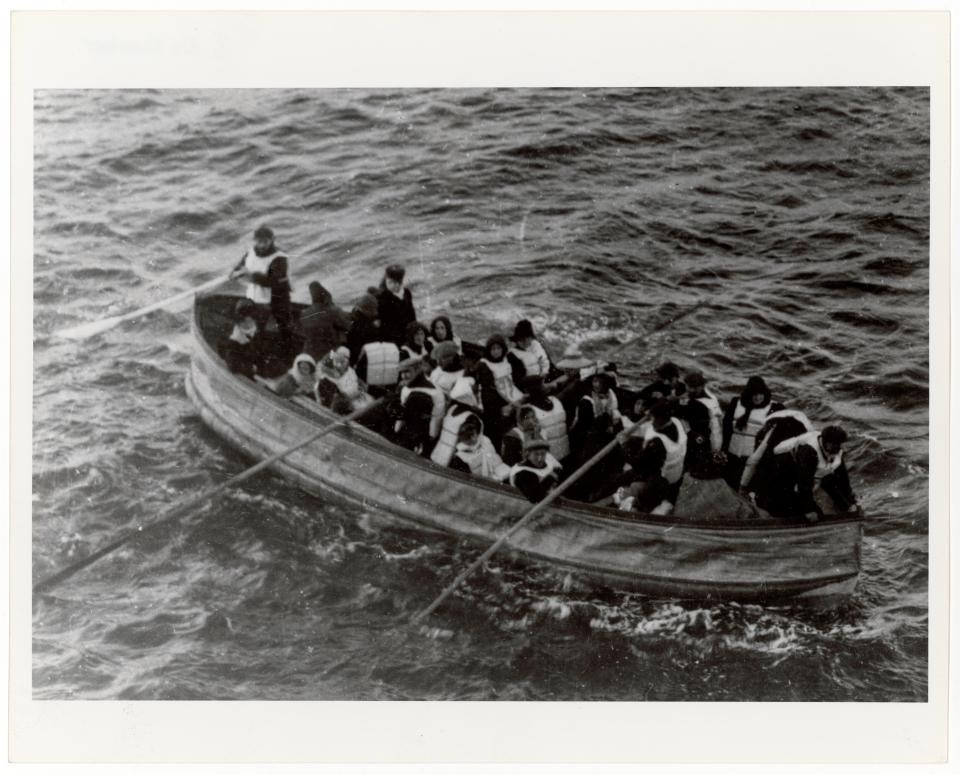 lifeboat with 4 long oars and perhaps 25 people, most wearing life vests 