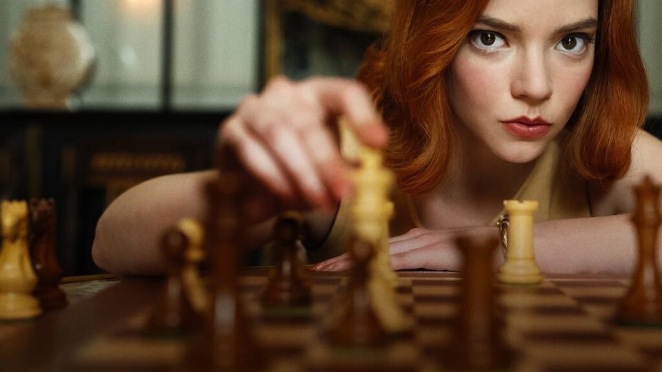 a woman with red hair moves a chess piece on a board