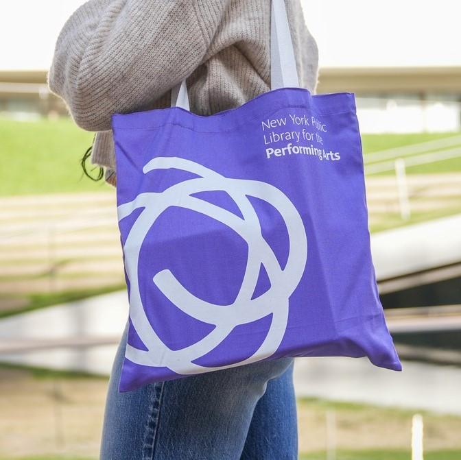 A person carries a purple tote bag that says New York Public Library for the Performing Arts