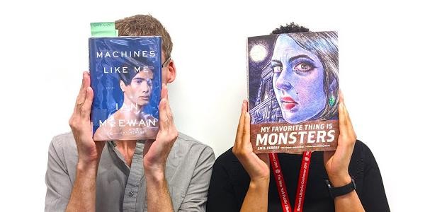 Two people holding book covers featuring faces up to their heads.