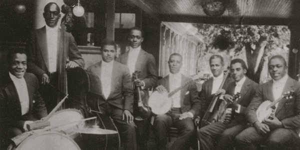 A group shot of James Reese Europe’s String Octett. The men are sitting down and holding instruments. One person is standing.