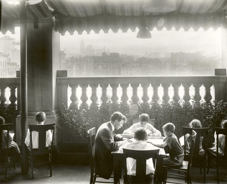 Boys sit around a table outside, with the city skyline visible behind them