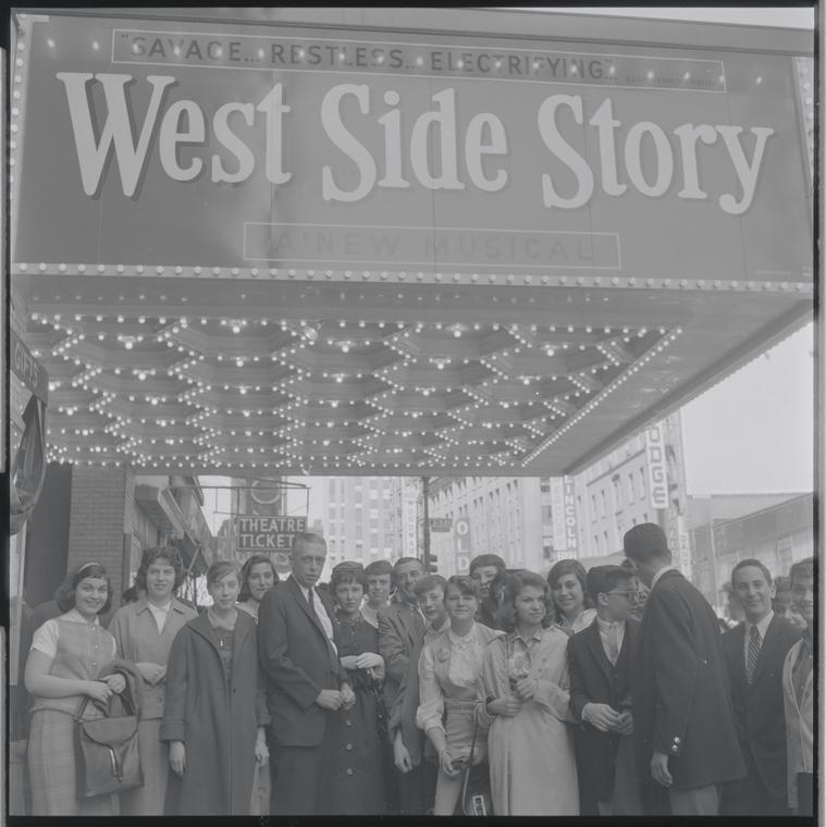 Students grouped together, standing in front of theatre with marquee reading "West Side Story"