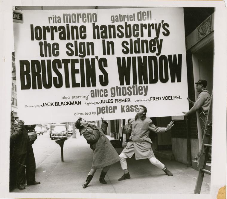 Actors Rita Moreno and Gabriel Dell posing beneath a theater marquee sign advertising their roles in Lorraine Hansberry's play The Sign in Sidney Brustein's Window at the Longacre Theatre in New York City.
