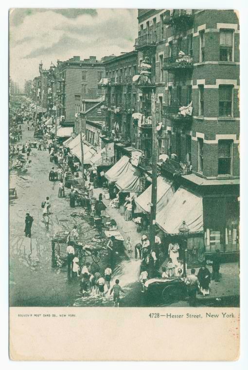 a postcard showing a street full of tenements flooded by a fire hydrant, with children playing in the water