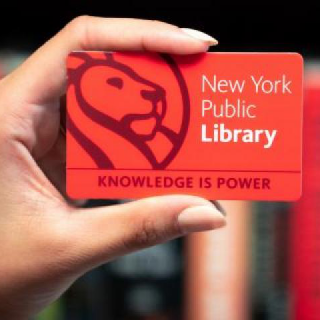 A hand holds a red library card featuring the words New York Public Library and Knowledge Is Power