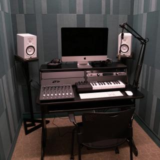 Small teal room with a recording studio setup including an iMac, a midi keyboard, two speakers, and a mixing table. 