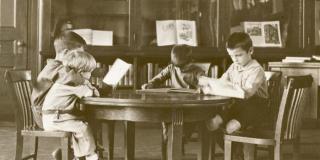 Black and white photograph of four children reading at a circular table.