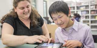 Visually impaired young man and librarian using a tablet to read a book.