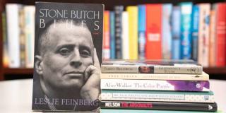 Cover of 'Stone Butch Blues,' featuring Leslie Feinberg, displayed next to a stack of library books.