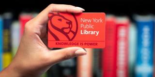 Hand holding a red NYPL card with text that reads: New York Public Library, Knowledge Is Power