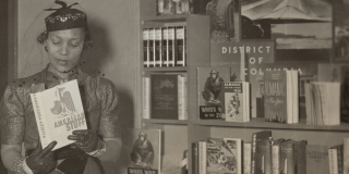 Historic photo of Zora Neale Hurston reading a book next to a bookshelf