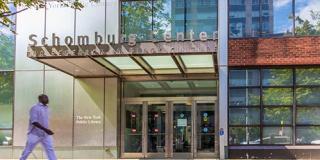 Exterior of the Schomburg Center in the sunshine with a person walking past the front of the building