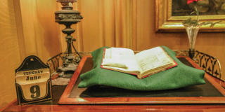 Photograph of Charles Dickens's desk, featuring a historic book on a piece of green felt next to a historic desk calendar