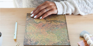 Photo of a Black woman's hand with painted fingernails and a tattooed ring resting on a notebook inspired by the Hunt Lenox Globe