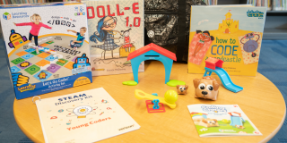 Photo of an NYPL Young Coders Kit spread out on a table with items including: Coding Critters robot set, Let’s Go Code game, and two books