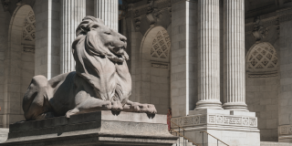 Photo of Patience the lion statue perched on a pedestal outside of the Stephen A. Schwarzman Building