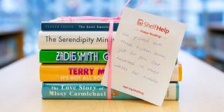 Stack of books tied with a pink ribbon and a handwritten note attached on paper that reads: Shelf Help, Happy Reading!