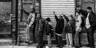 A group of young children standing against the side of building raising their left arms in the Black power stance. 