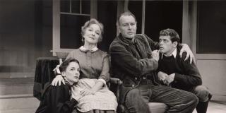 A black and white archival image of two younger people kneeling down and being clutched tenderly by two central older people.