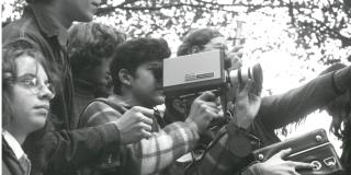 A black and white photo of six young people using old cameras looking off the image.
