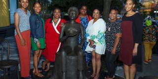 Eight Black women librarians stand in formation around a statue of Lorraine Hansberry in front of the Schomburg Center