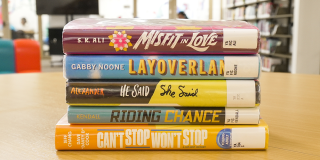 Photo of a stack of young adult books including titles like, Misfit in Love, Layoverland, He Said She Said, Riding Chance, and Can't Stop Won't Stop. 