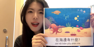 A woman leading a storytime holds up a children's book showing Mandarin text and an undersea scene.