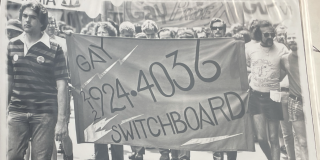Archival image of people holding a Gay Switchboard banner in a street demonstration.