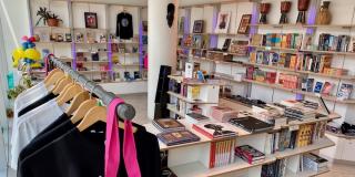 Interior of the Schomburg Shop featuring a rack of clothing in the foreground, a table displaying books in the midground, and shelving displaying books and art in the background.
