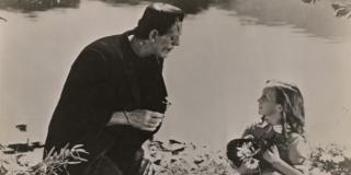 Still from film adaptation of Frankenstein showing Frankenstein's monster holding a flower and talking to a young girl.