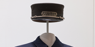 Brotherhood of Sleeping Car Porters uniform; hat affixed above a collared jacket on a dressform with folded pants hanging beneath the jacket, all navy blue