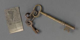 Photo of a small black-and-white newspaper clipping next to a set of large bronze keys.
