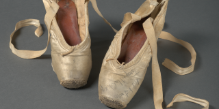 Peach satin pointe shoes with signs of wear, darned toes, and untied ribbons. The shoe at right bears the handwritten inscription “All best wishes, Tanaquil Le Clerq”