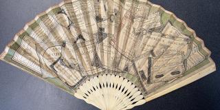 a paper fan decorated with what appears to be a pile of trompe l’oeil assignats viewed from above