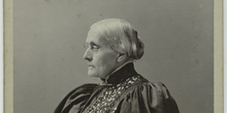 Cabinet card featuring black-and-white photograph of Susan B. Anthony seated and holding a book, looking to her right and wearing a dress with puffed sleeves