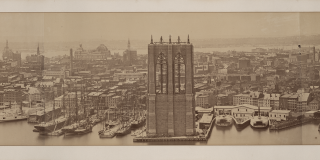 Wide, panoramic, sepia-toned photograph showing the construction of one of the Brooklyn Bridge’s tours and an expanse of the island of Manhattan