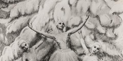A black and whit photo of 5 dancers dressed as snowflakes forming a circle with their arms. A tree covered in snow is in the background.