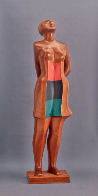 A wooden statue of a woman gazing upward, with color blocked panels on her torso