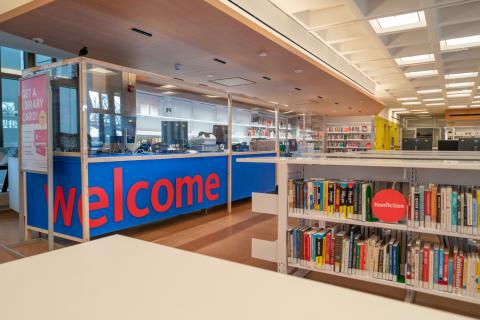 Photo of the interior of the new Roosevelt Island Library featuring an information desk with a large blue banner with red text that reads: Welcome 